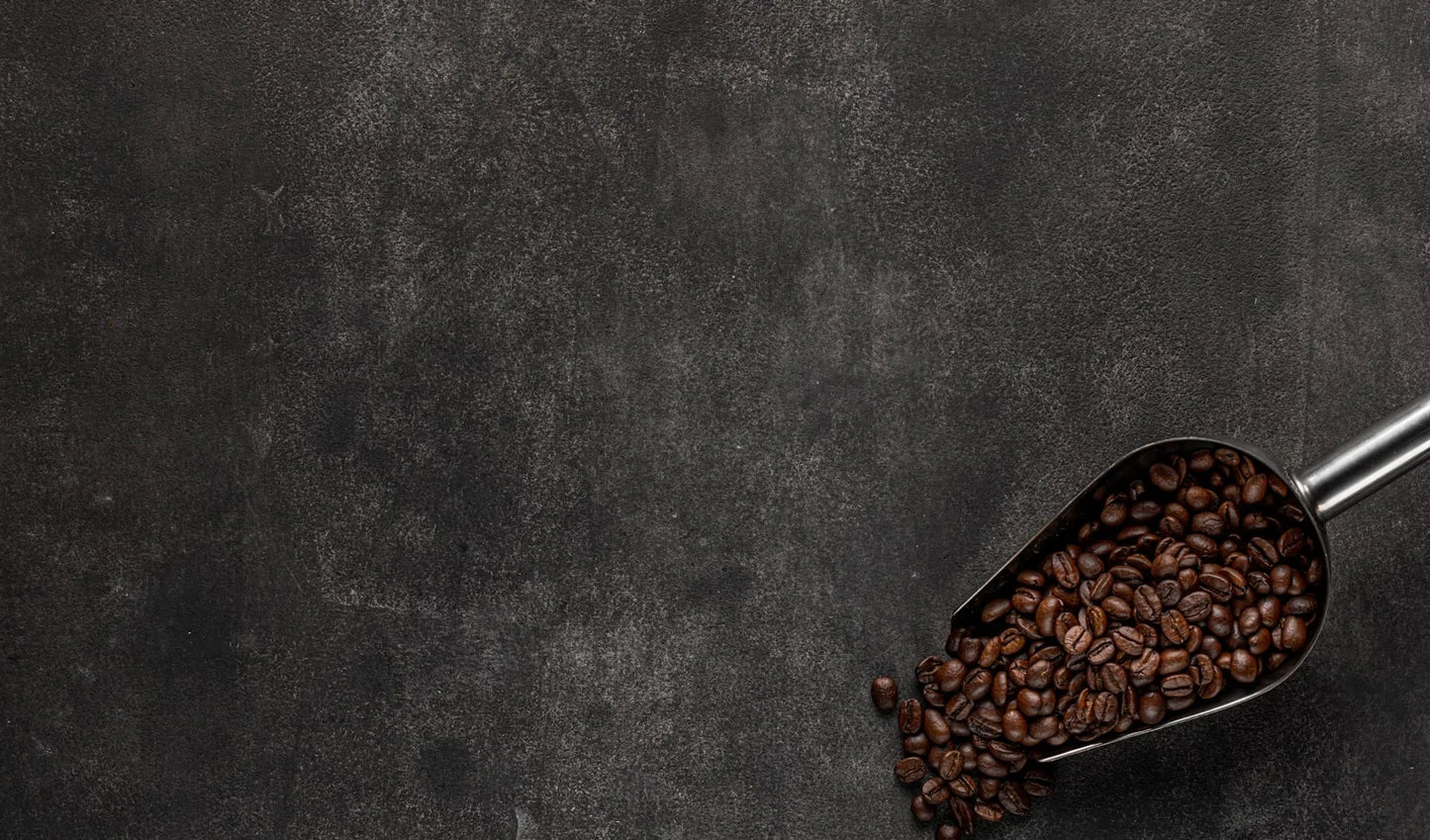 reshly roasted coffee beans in a metal scoop on a dark surface