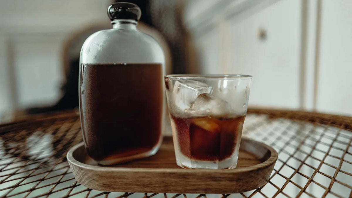 Cold brew koffie geserveerd in een glas met ijs naast een karaf concentraat