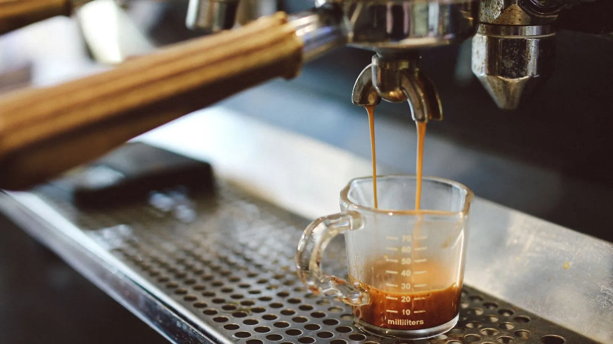 Espresso loopt uit de zeef in een klein glazen maatbekertje op een espressomachine.