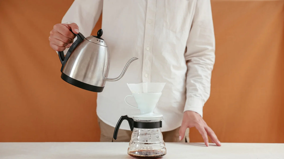 Hand giet heet water uit een tuitketel over een filterkoffie-dripper